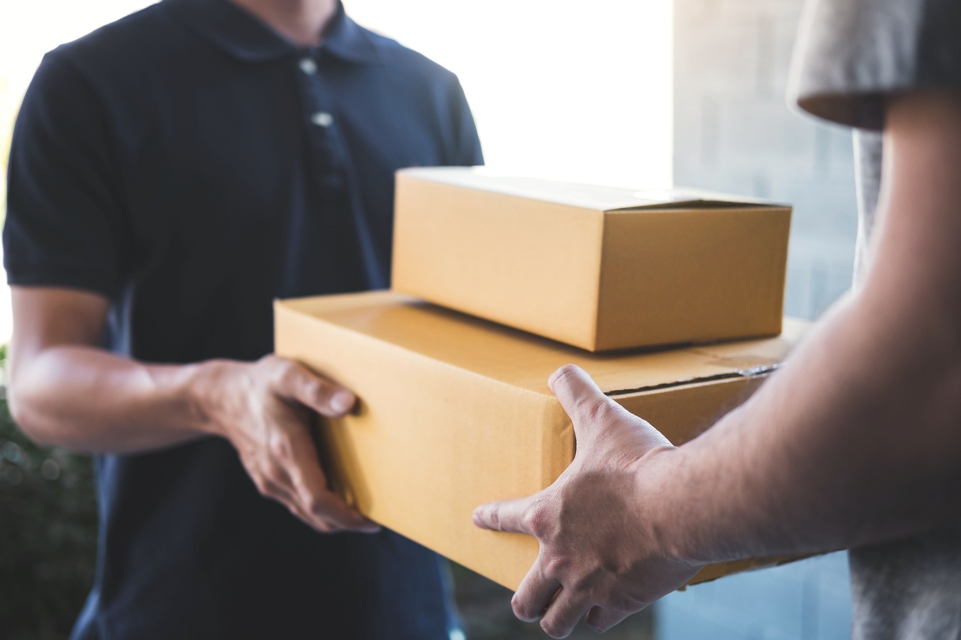 Midsection Of Delivery Person Giving Boxes To Young Man At Home