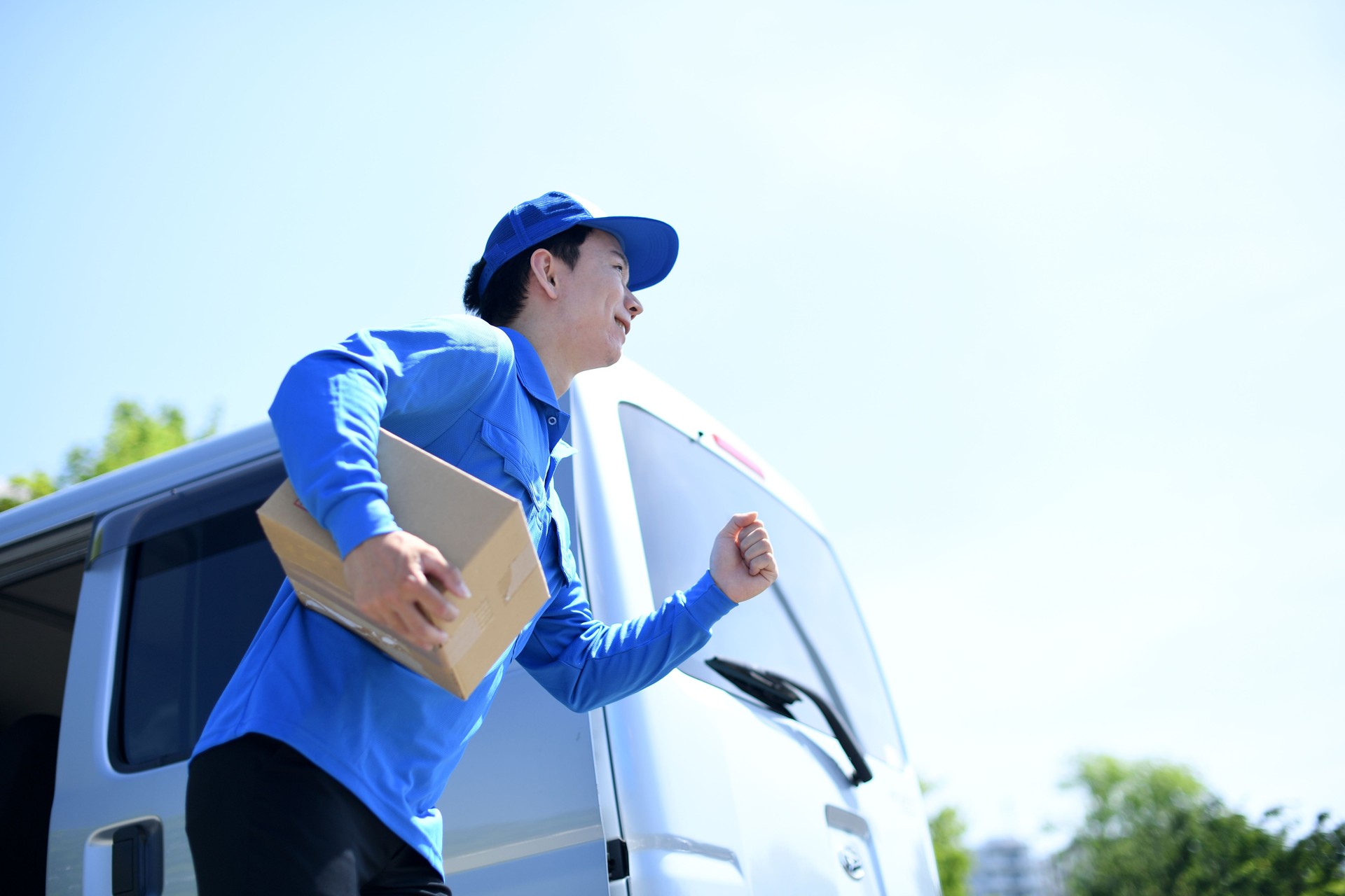 Under the blue sky, an Asian male delivery driver runs energetically and delivers packages.